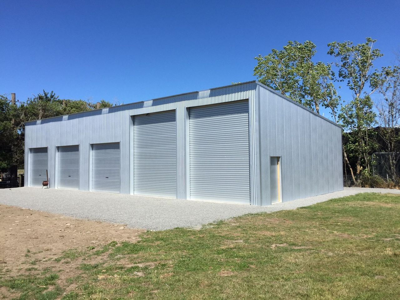 A large metal building with three garage doors is sitting in the middle of a grassy field.