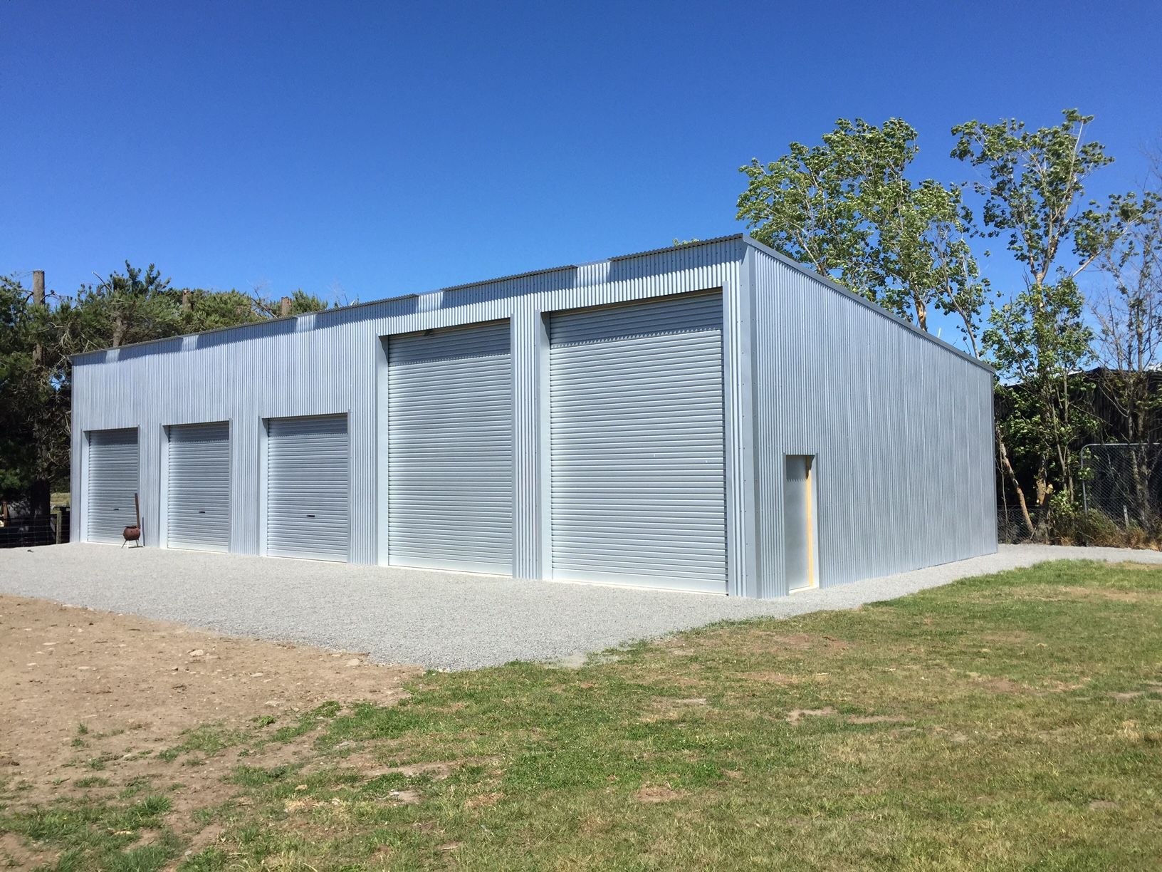 A large metal building with three garage doors is sitting in the middle of a grassy field.