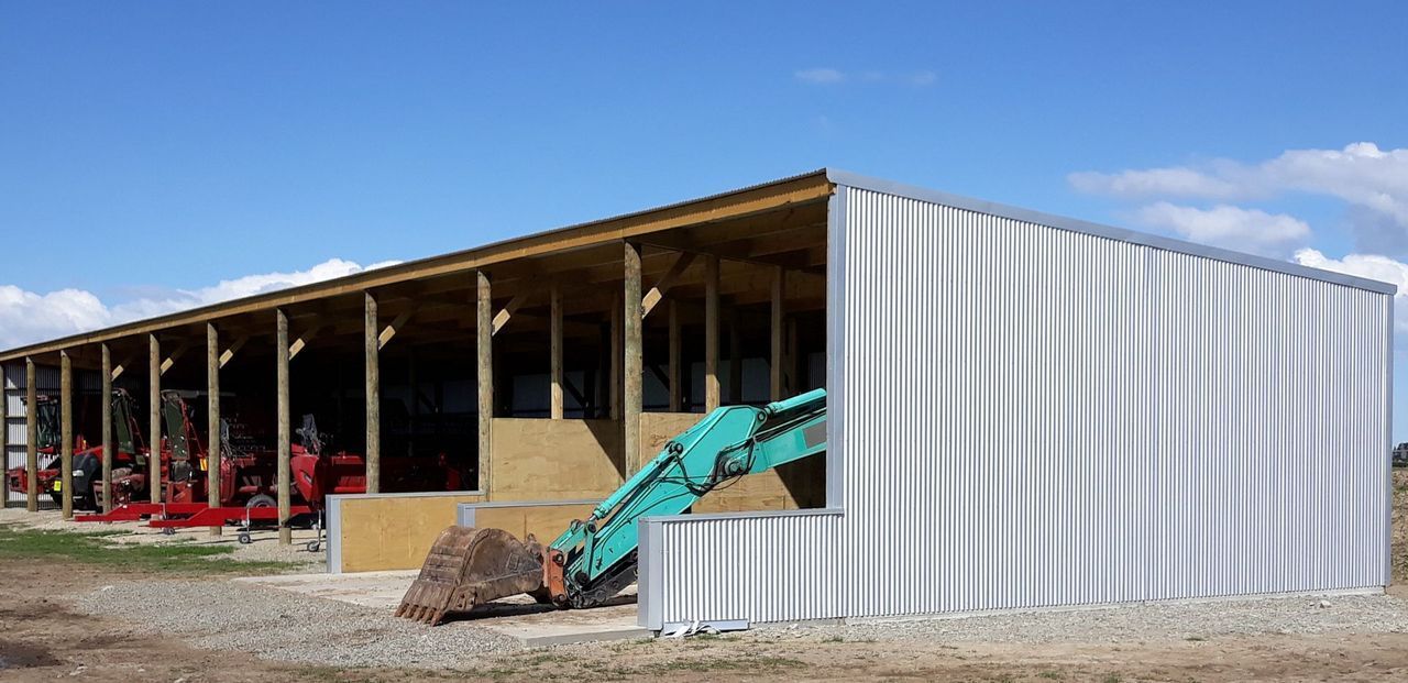 A green excavator is parked in front of a white building.