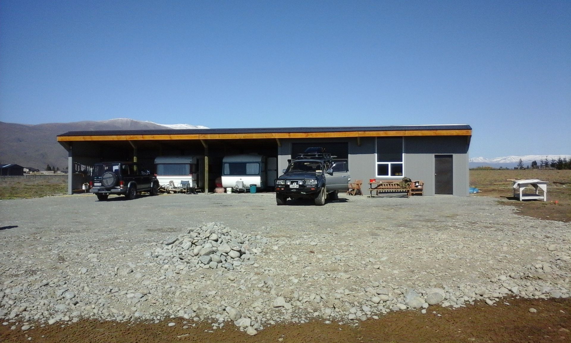Two cars are parked in front of a house with mountains in the background