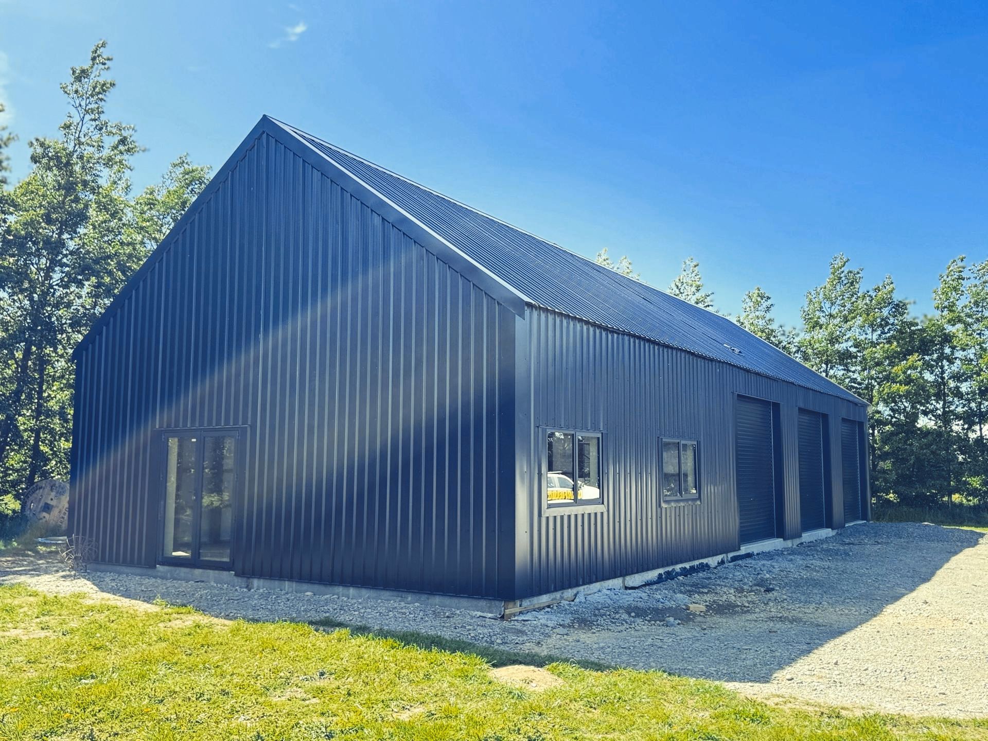 A large black building with a roof that looks like a barn is sitting in the middle of a grassy field.
