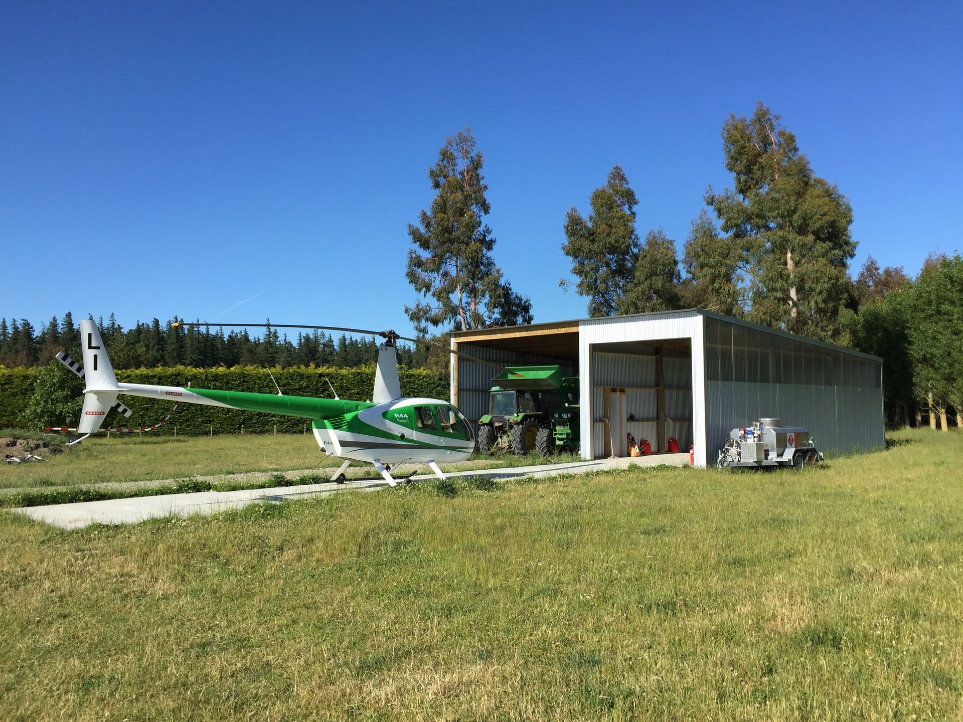 A small green and white plane is parked in front of a hangar.