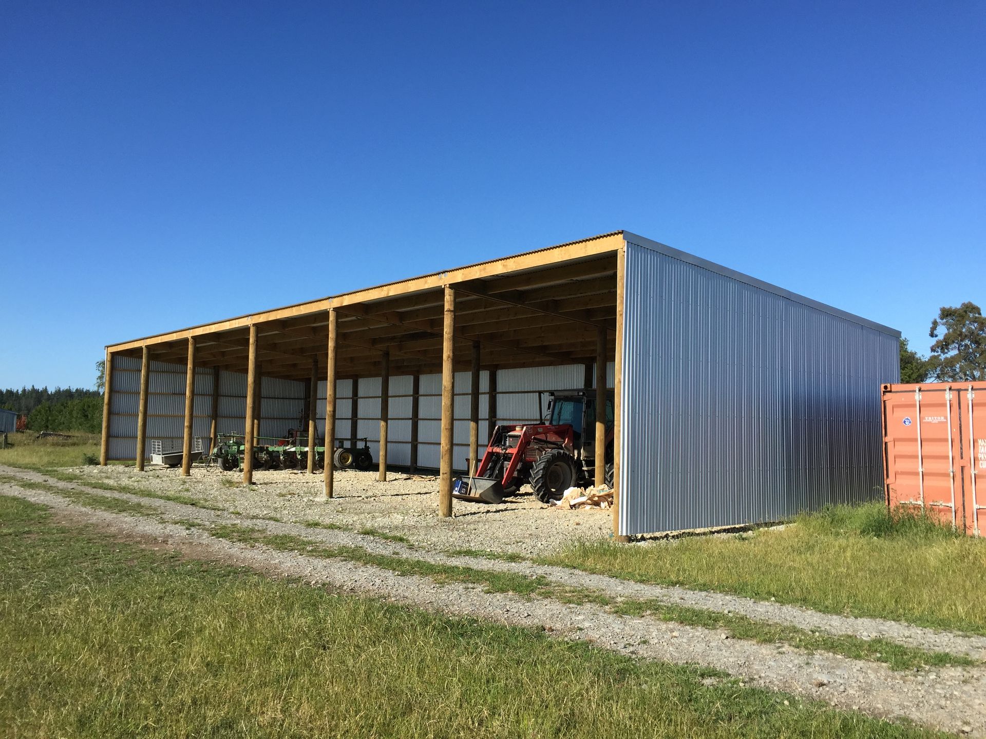 A tractor is parked under a shed in a field.