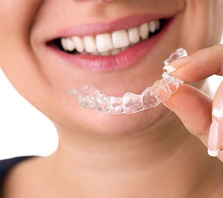 Invisalign — Smiling Female Holding Transparent Teeth Braces in Tenafly, NJ