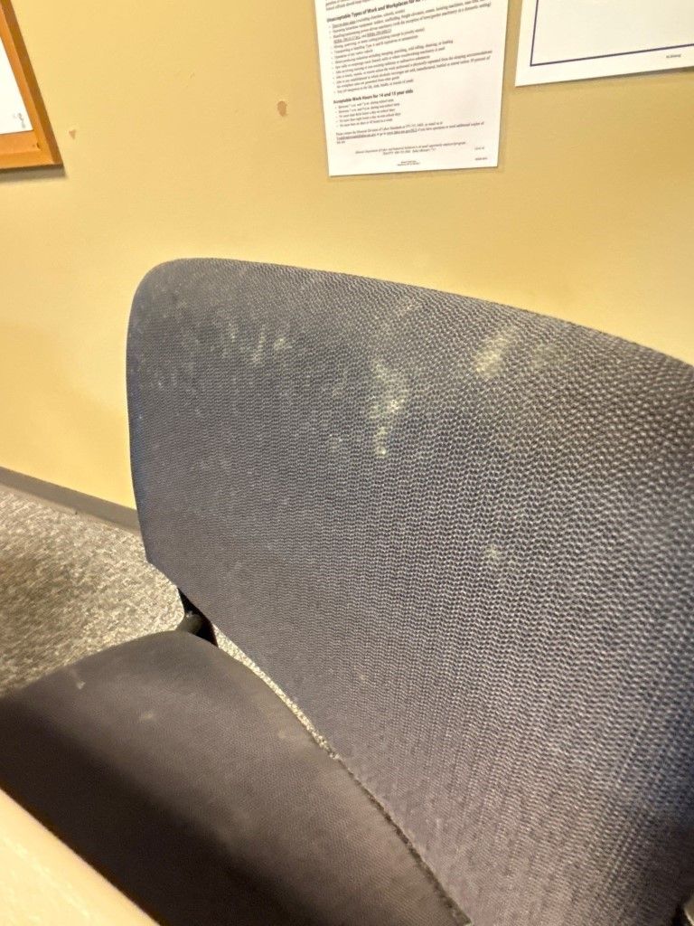 A dirty chair in front of a wall with papers on it