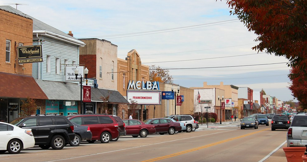 A row of cars are parked in front of a melba theater