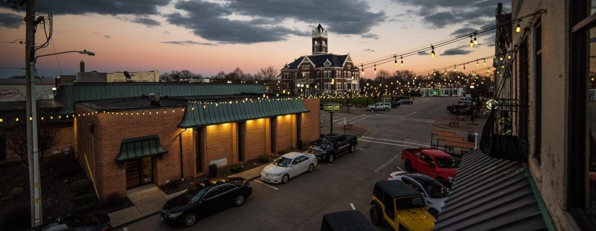 An aerial view of a city street at sunset with cars parked on the side of the road.