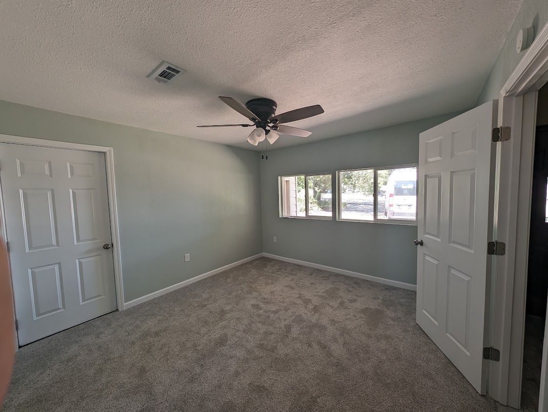 An empty bedroom with a ceiling fan and three windows.