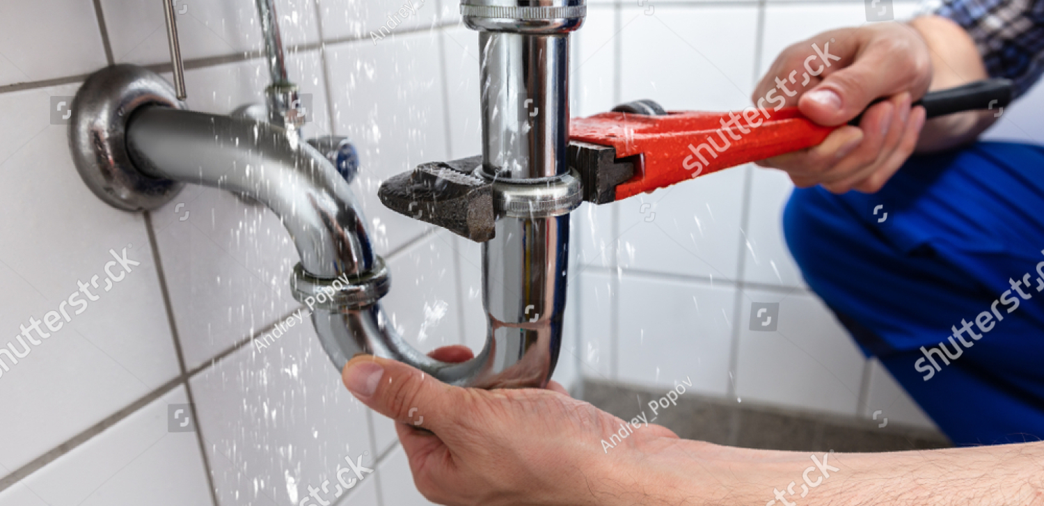 A plumber is fixing a pipe in a bathroom with a wrench.