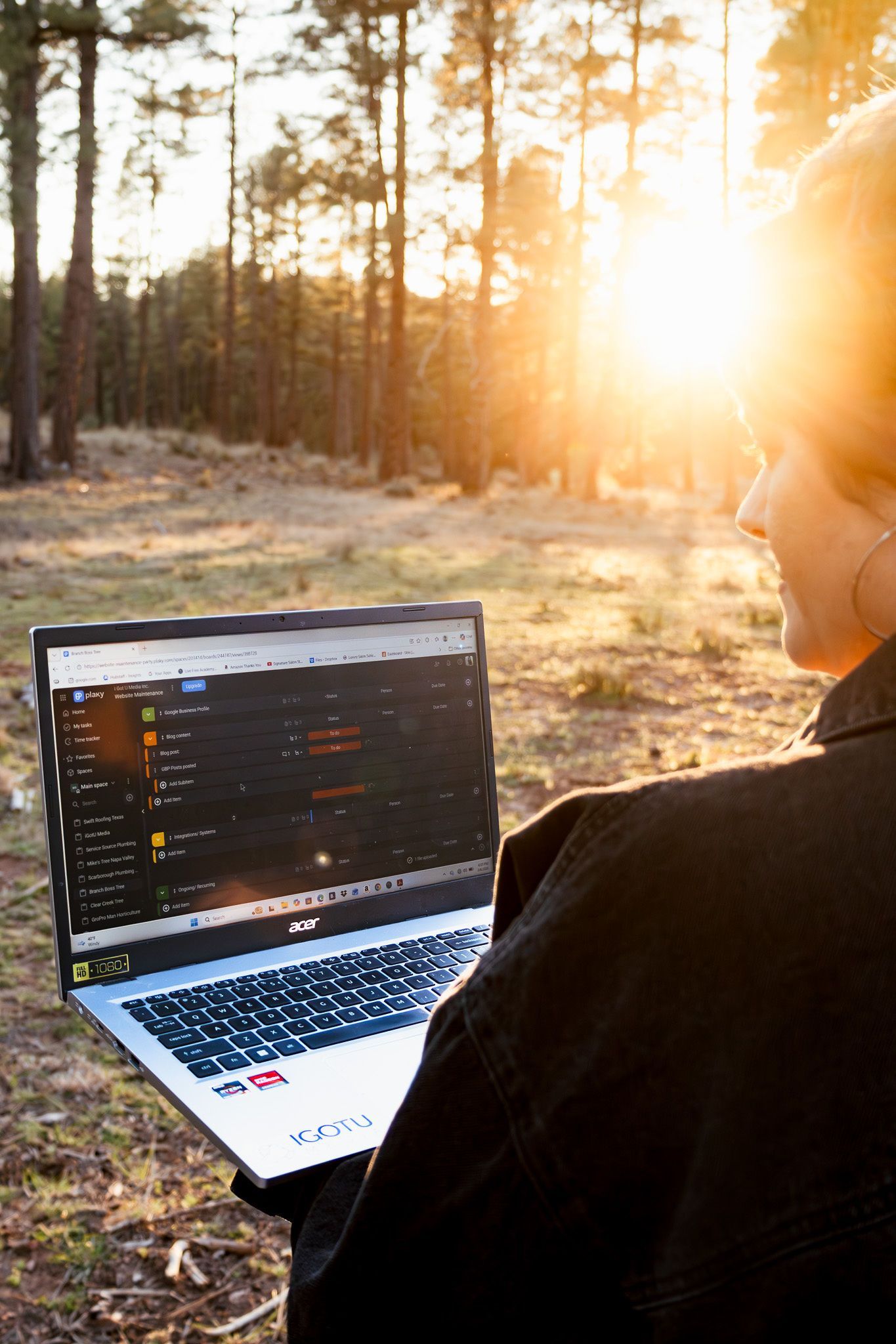 Person using a laptop outdoors in a sunlit forest at sunset