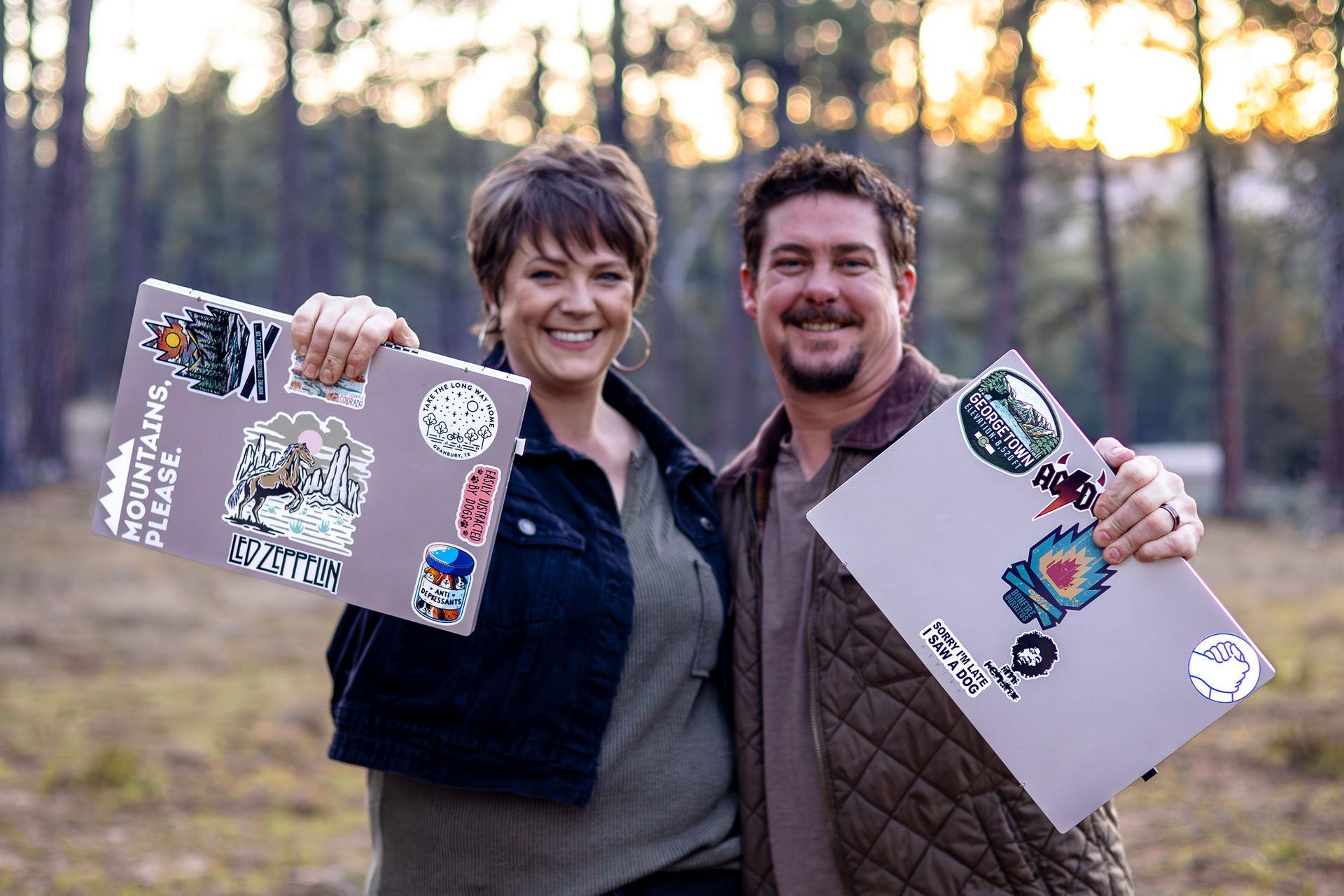 Two people smiling outdoors at sunset, holding decorated laptop covers