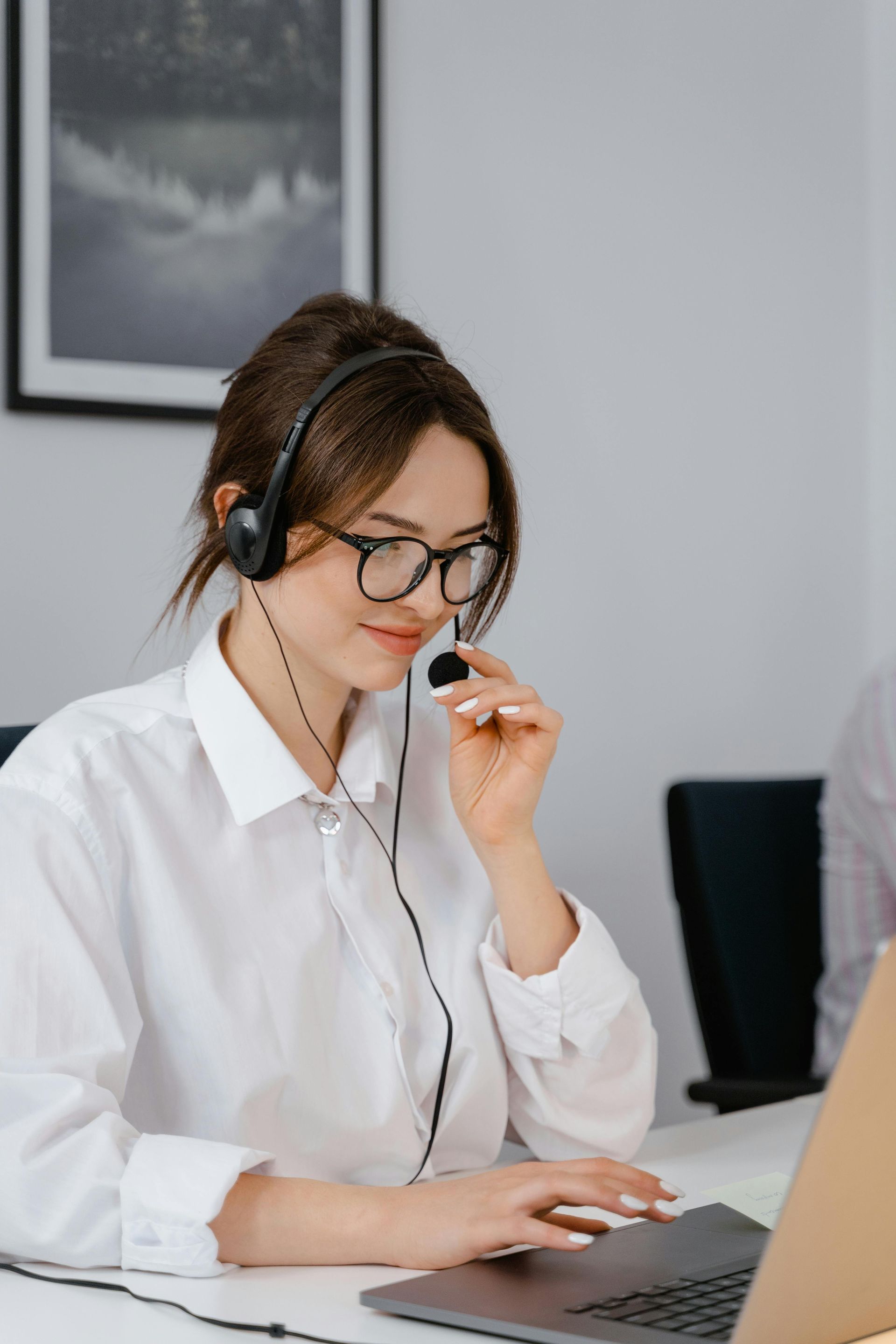A woman wearing headphones and glasses is sitting in front of a laptop computer.