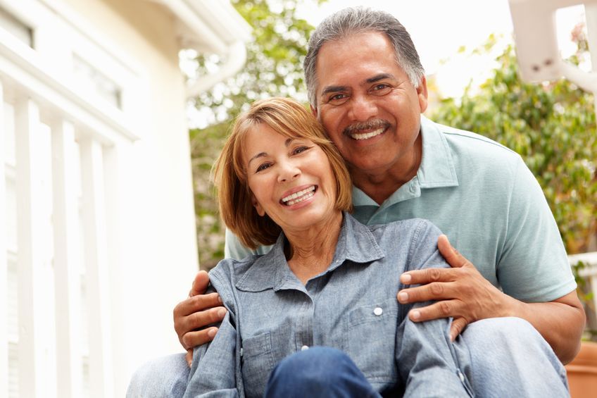 Smiling couple embracing outdoors. Woman in blue shirt, man in green, natural light.