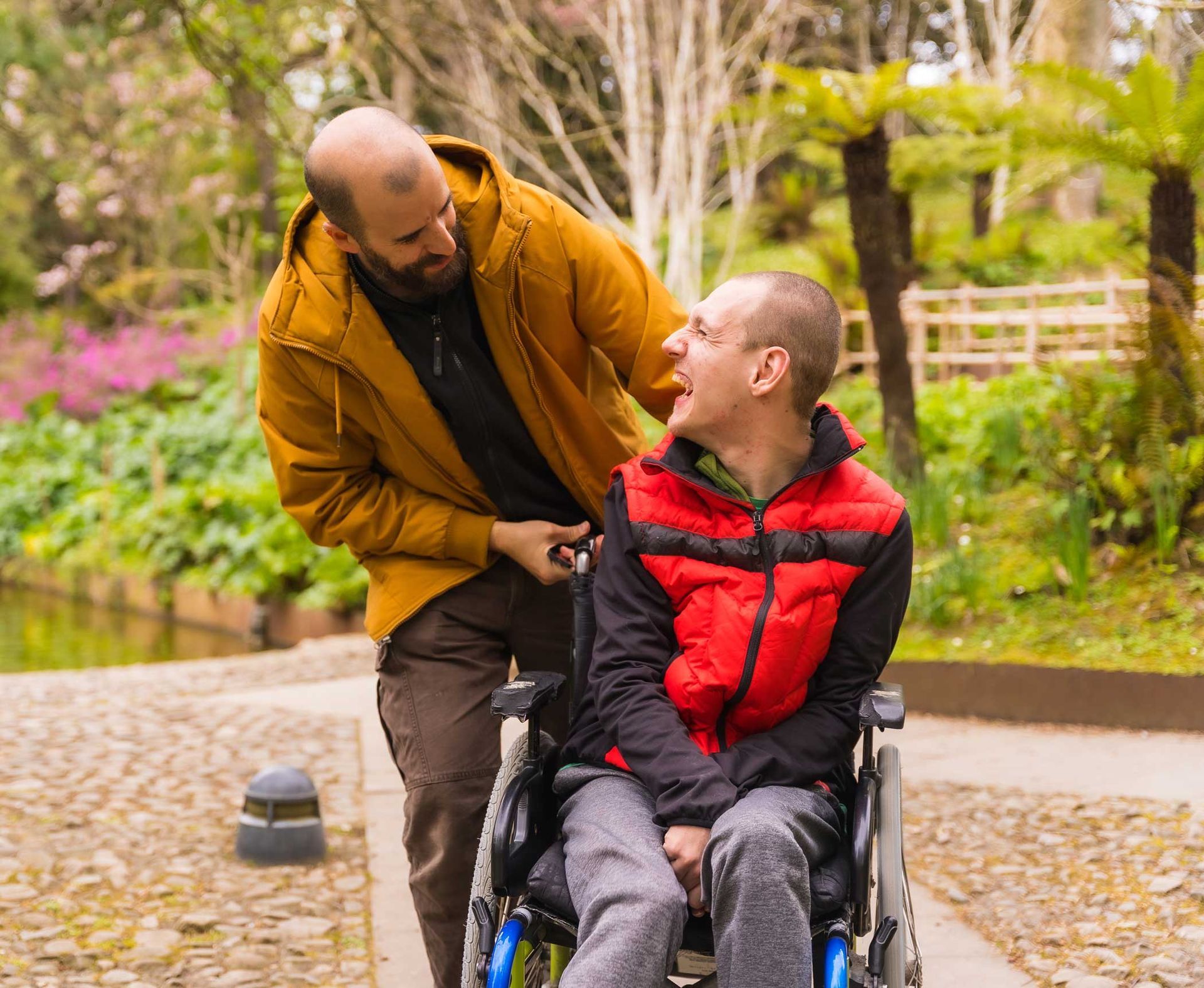 A person with a disability in a wheelchair laughing with a carer in a public park.