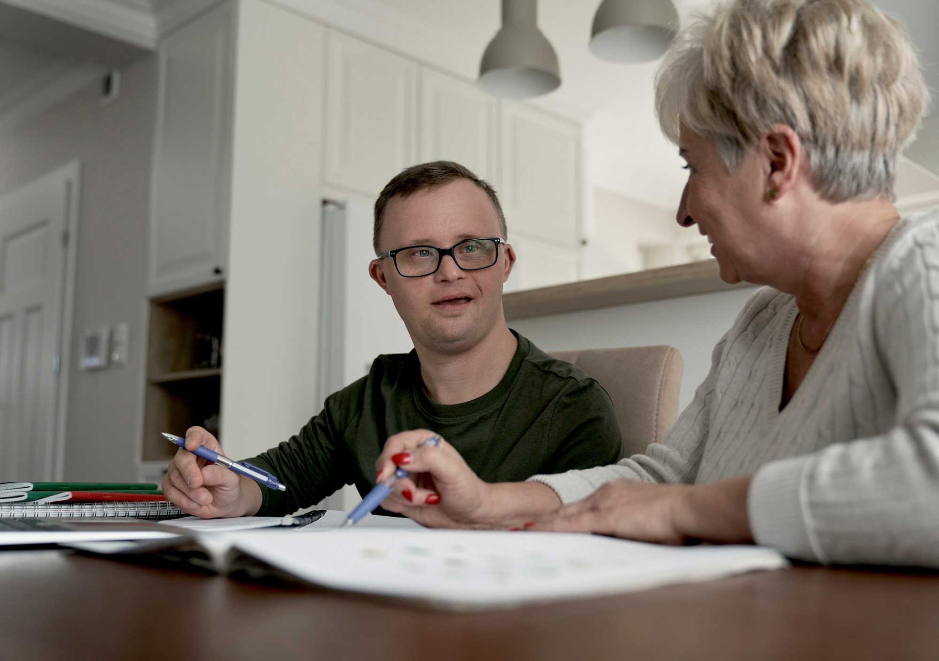 View of a man with Down Syndrome being taught by an older lady inside a house. View of a man with Down Syndrome being taught by an older lady inside a house.