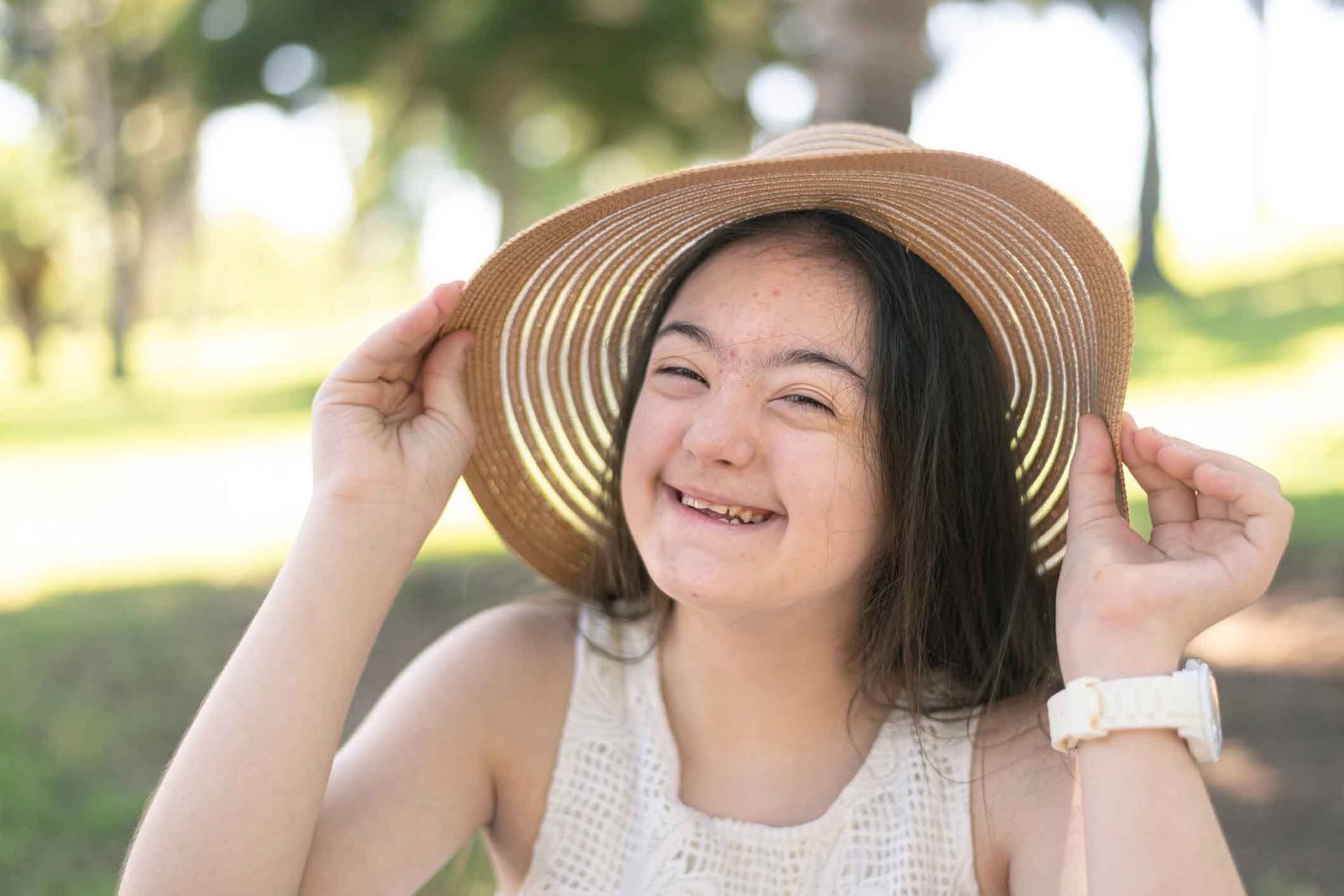 Young woman with Down syndrome smiling, wearing a sun hat in a park setting. Young woman with Down syndrome smiling, wearing a sun hat in a park setting.