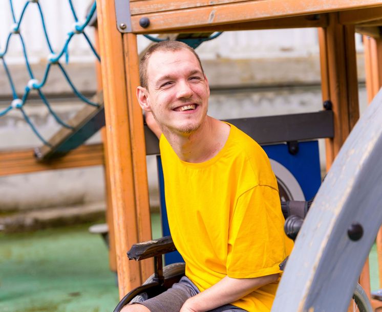 Smiling man in a yellow shirt and wheelchair at a playground, looking toward the left. Smiling man in a yellow shirt and wheelchair at a playground, looking toward the left.