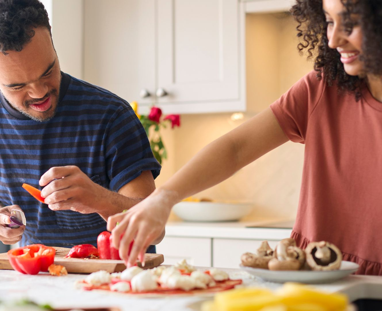 A man and woman prepare together a homemade pizza, inside a kitchen.