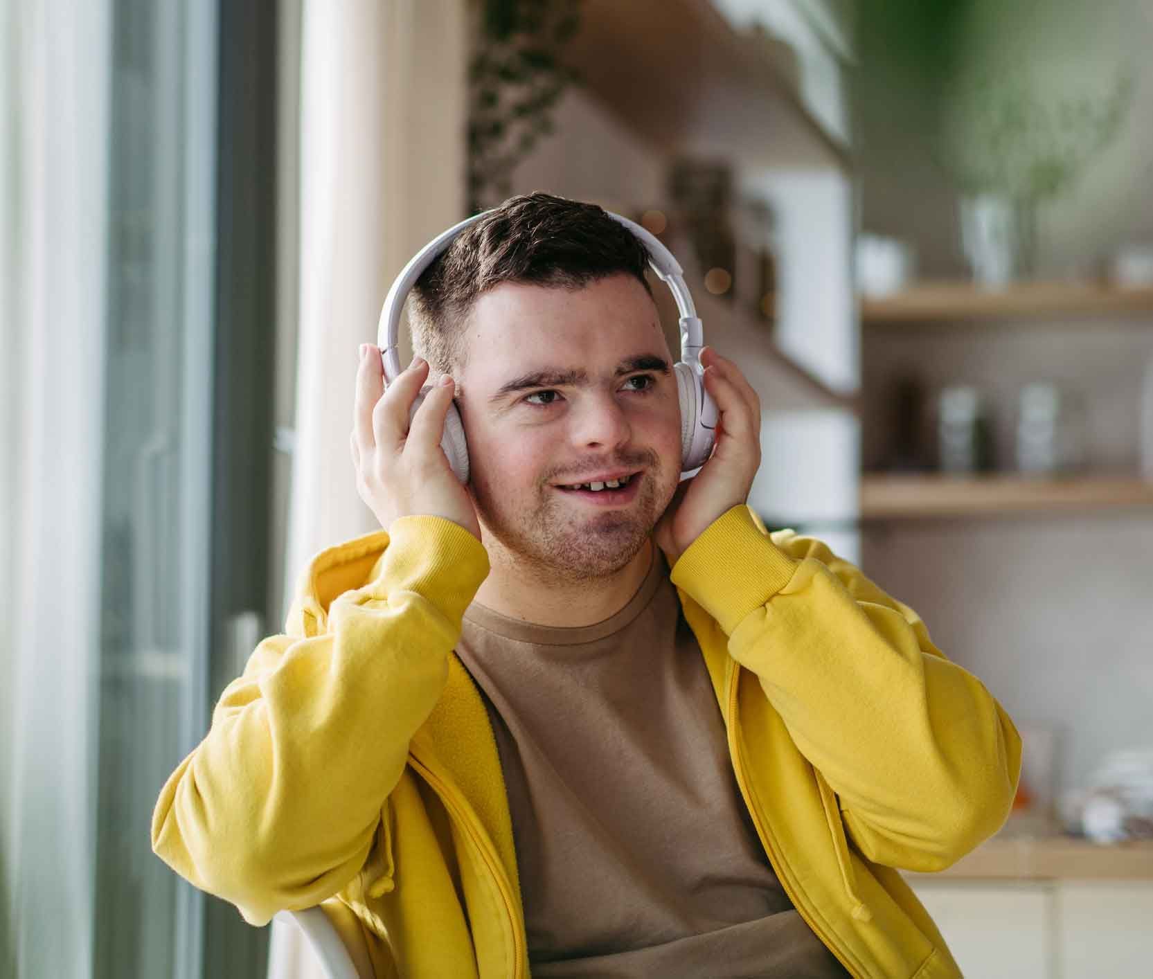 A man with Down syndrome wearing a yellow jacket and headphones, smiling while looking to the right.