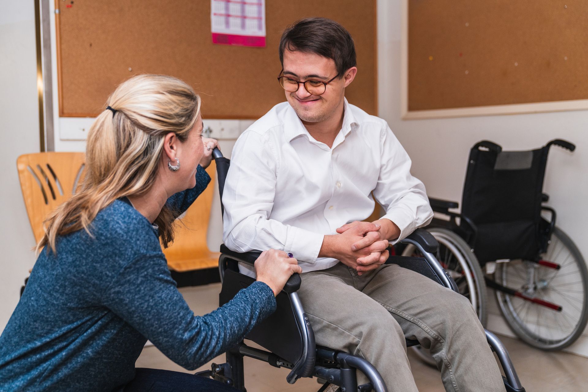 Female support worker speaks to a smiling man in a wheelchair.>
