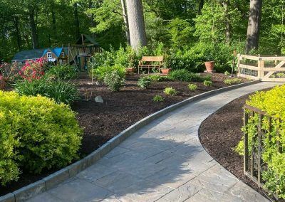 A walkway in a garden with a playground in the background