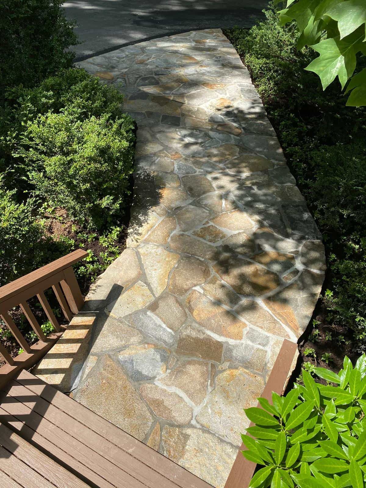 A stone walkway leading to a wooden deck surrounded by trees and bushes.