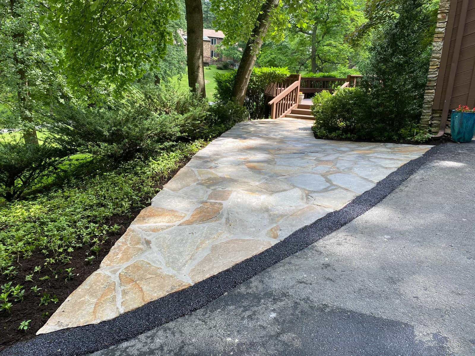 A stone walkway leading to a house with trees in the background.