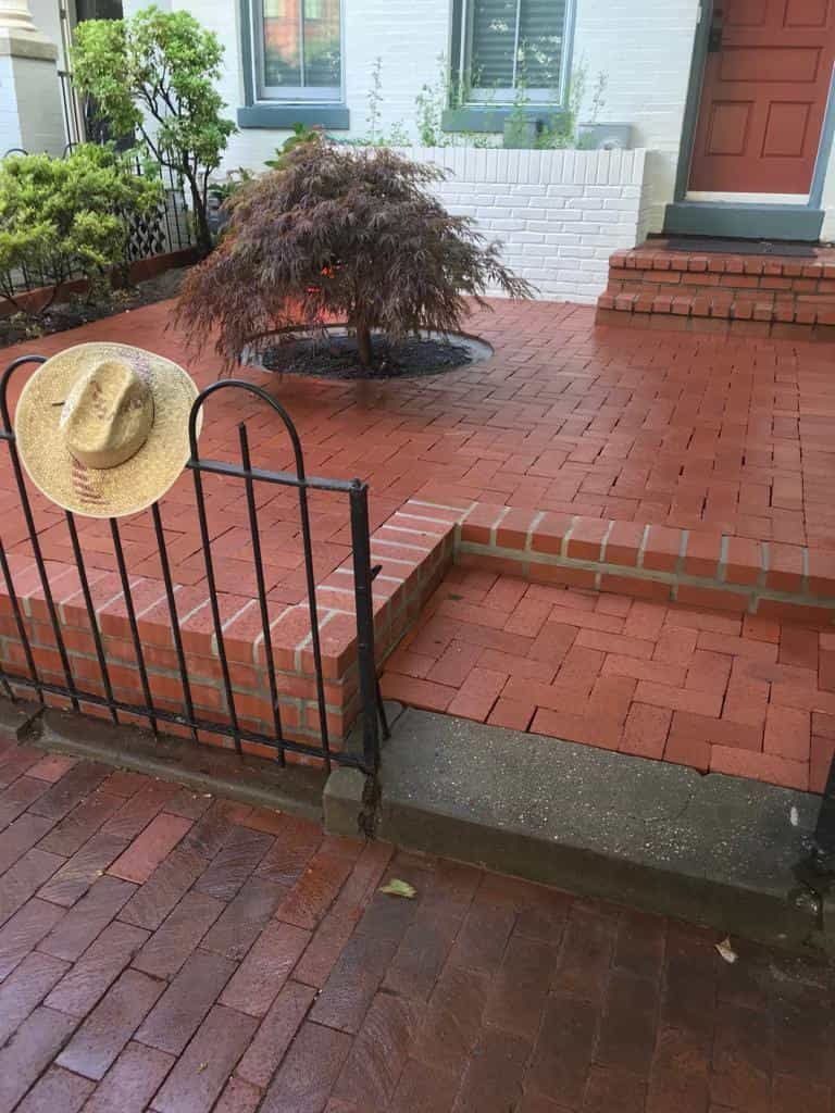 A straw hat is sitting on a fence next to a brick walkway.