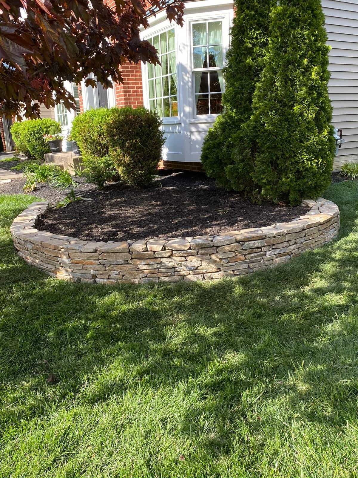 A stone wall in the middle of a lush green lawn in front of a house.