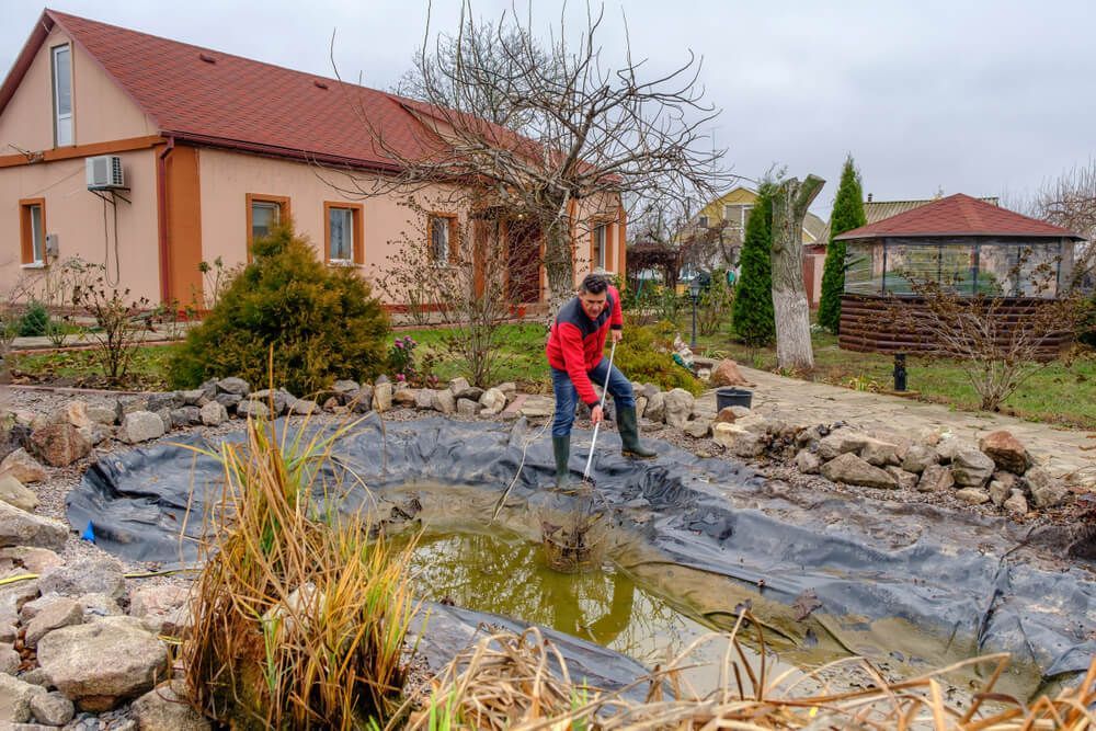 A man is digging in a pond in front of a house.