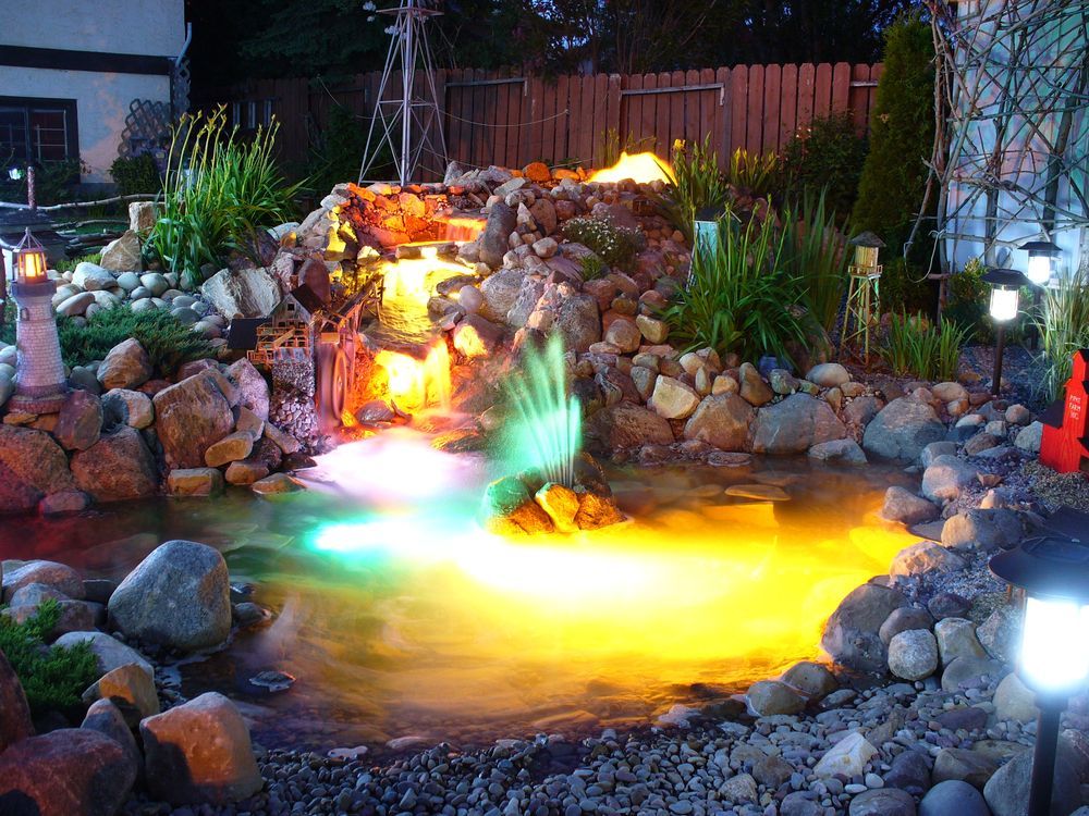 A waterfall is lit up at night in a backyard