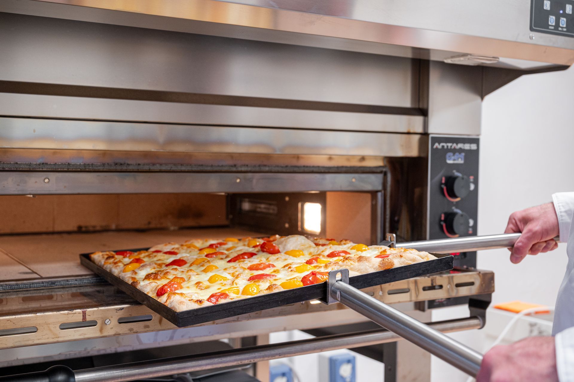 Pizza estratta da un forno professionale con pala e vassoio in metallo.