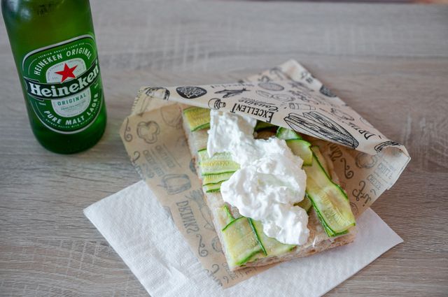 Una bottiglia di birra Heineken accanto a un wrap con lattuga su un tovagliolo, guarnito con una salsa simile alla panna montata.