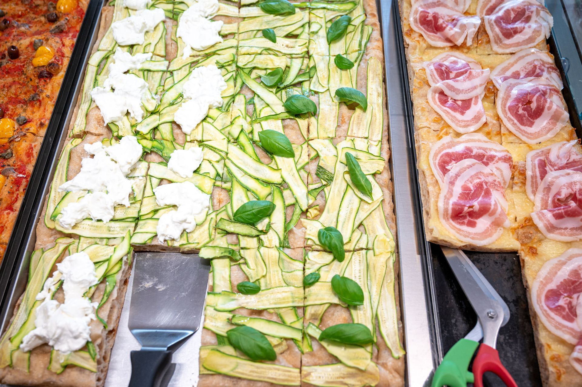 Vassoi di cibo già pronto: condimenti a base di patate e verdure, con pinze e affettati a portata di mano.