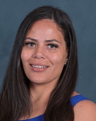 A woman with long hair is wearing a blue tank top and smiling for the camera.