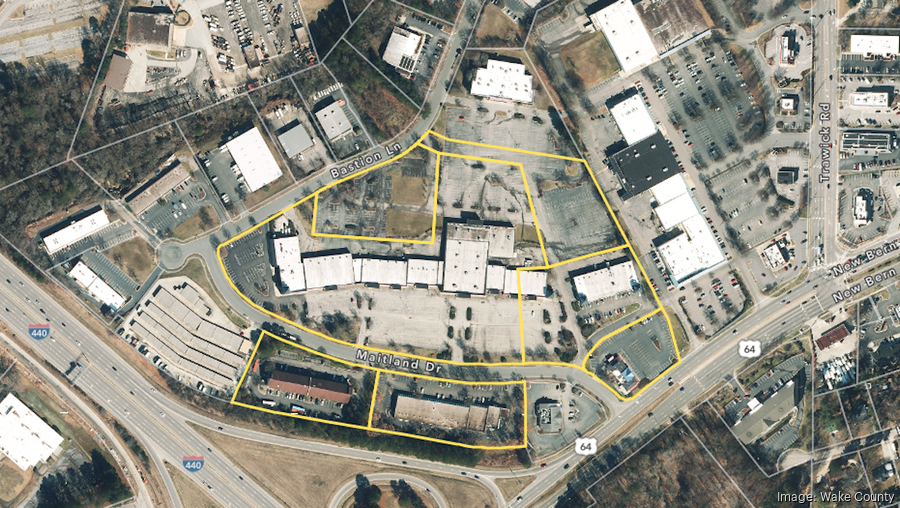 Aerial view of a commercial area, outlined in yellow. Includes buildings, parking lots, and roadways.