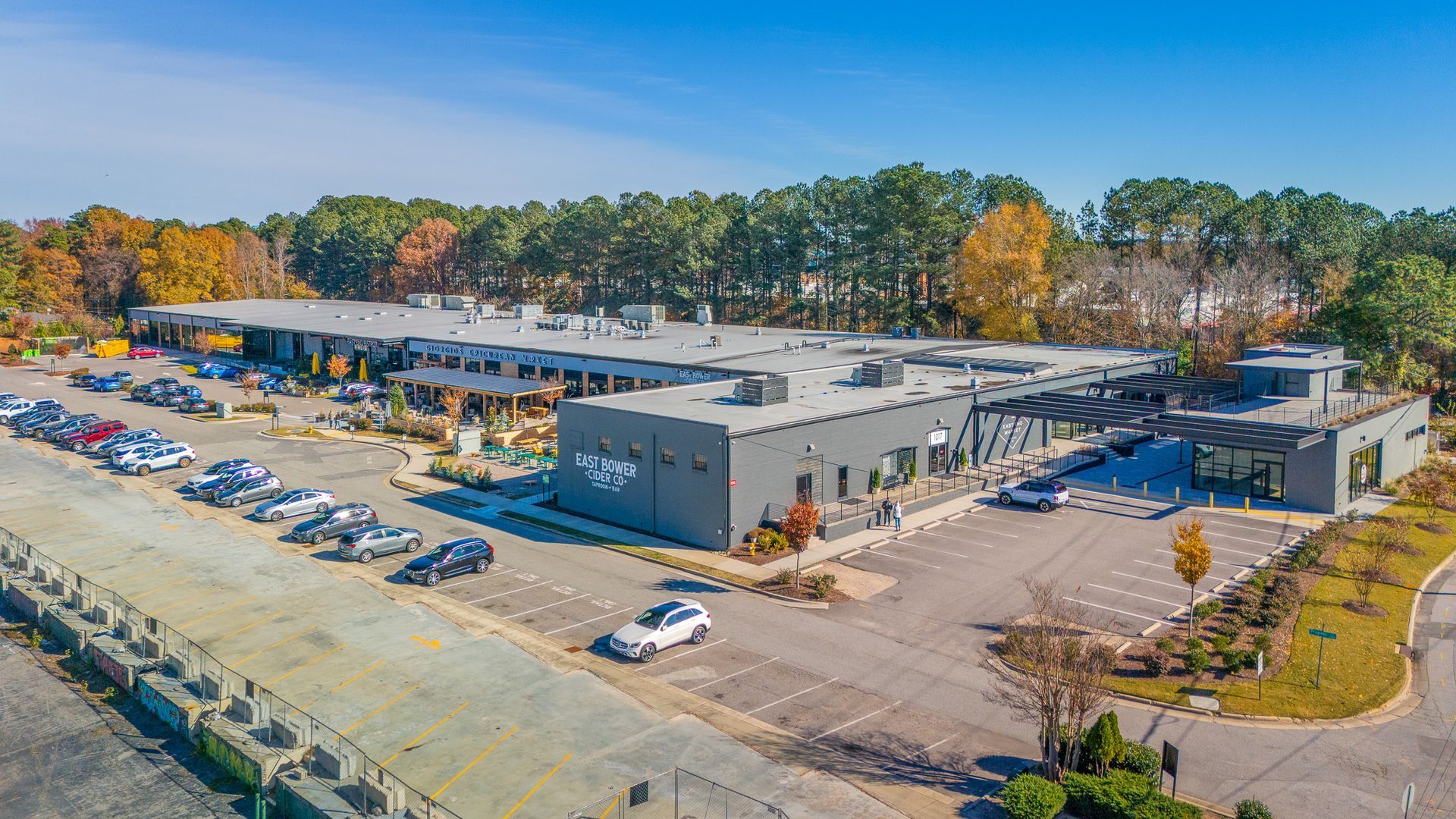 Exterior view of a modern gray building with cars parked in a lot. Trees in background under a blue sky.
