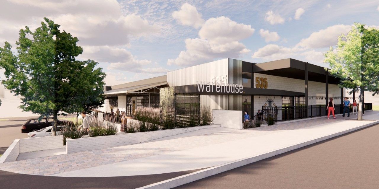 Exterior view of a modern building with a restaurant/cafe, featuring a black awning and outdoor seating.