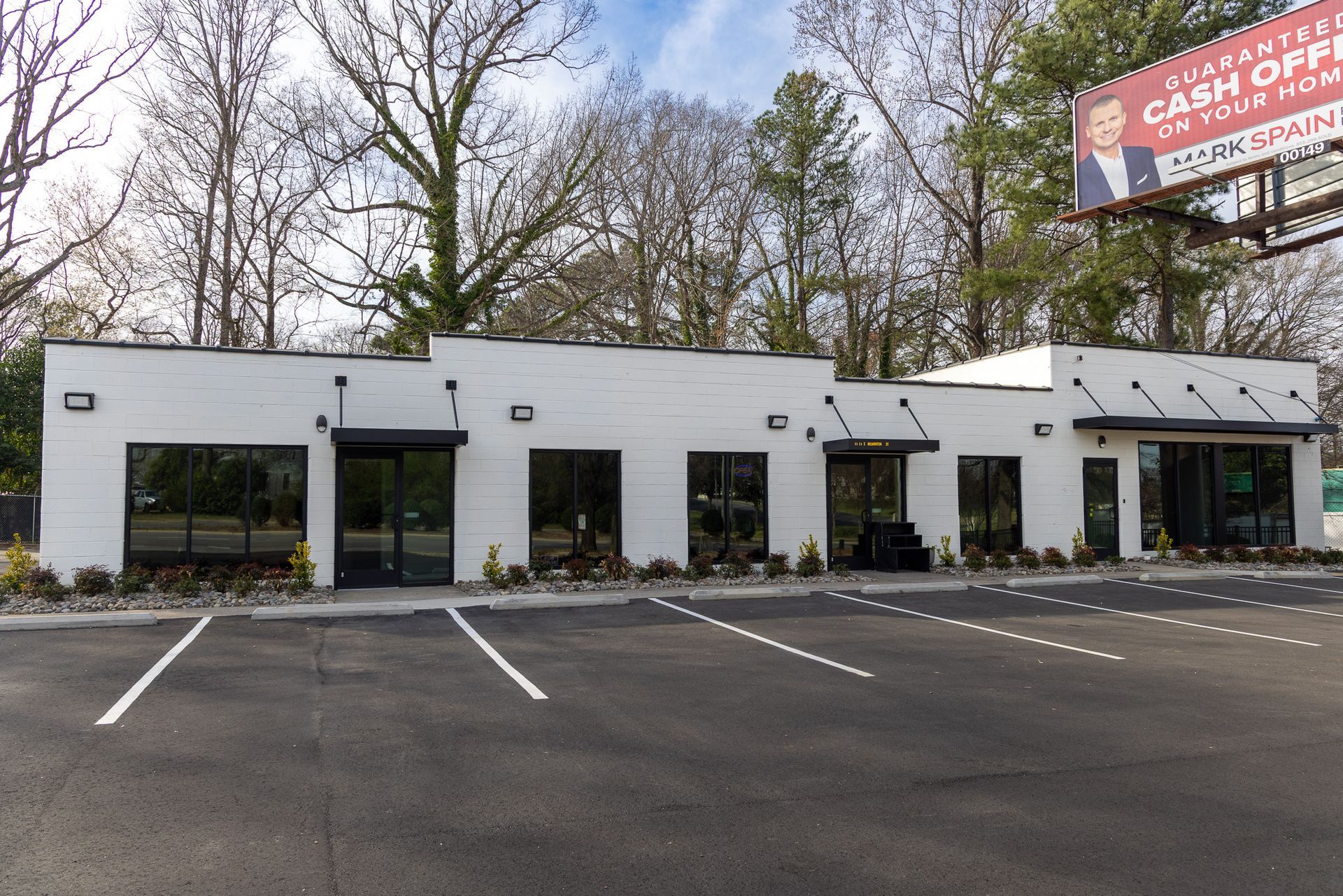 White brick commercial building with black awnings, large windows, and parking spaces.