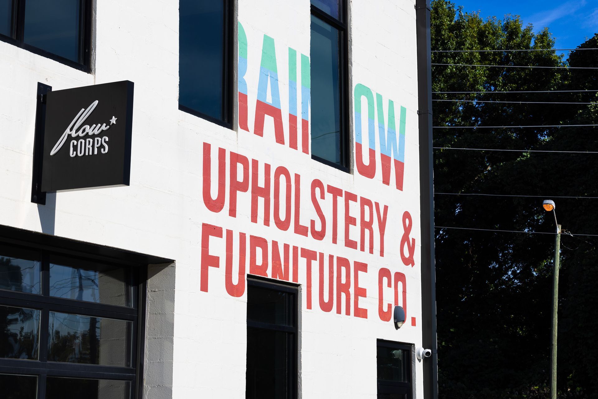 Building exterior: Rainbow Upholstery & Furniture Co. sign on white wall, black sign for 