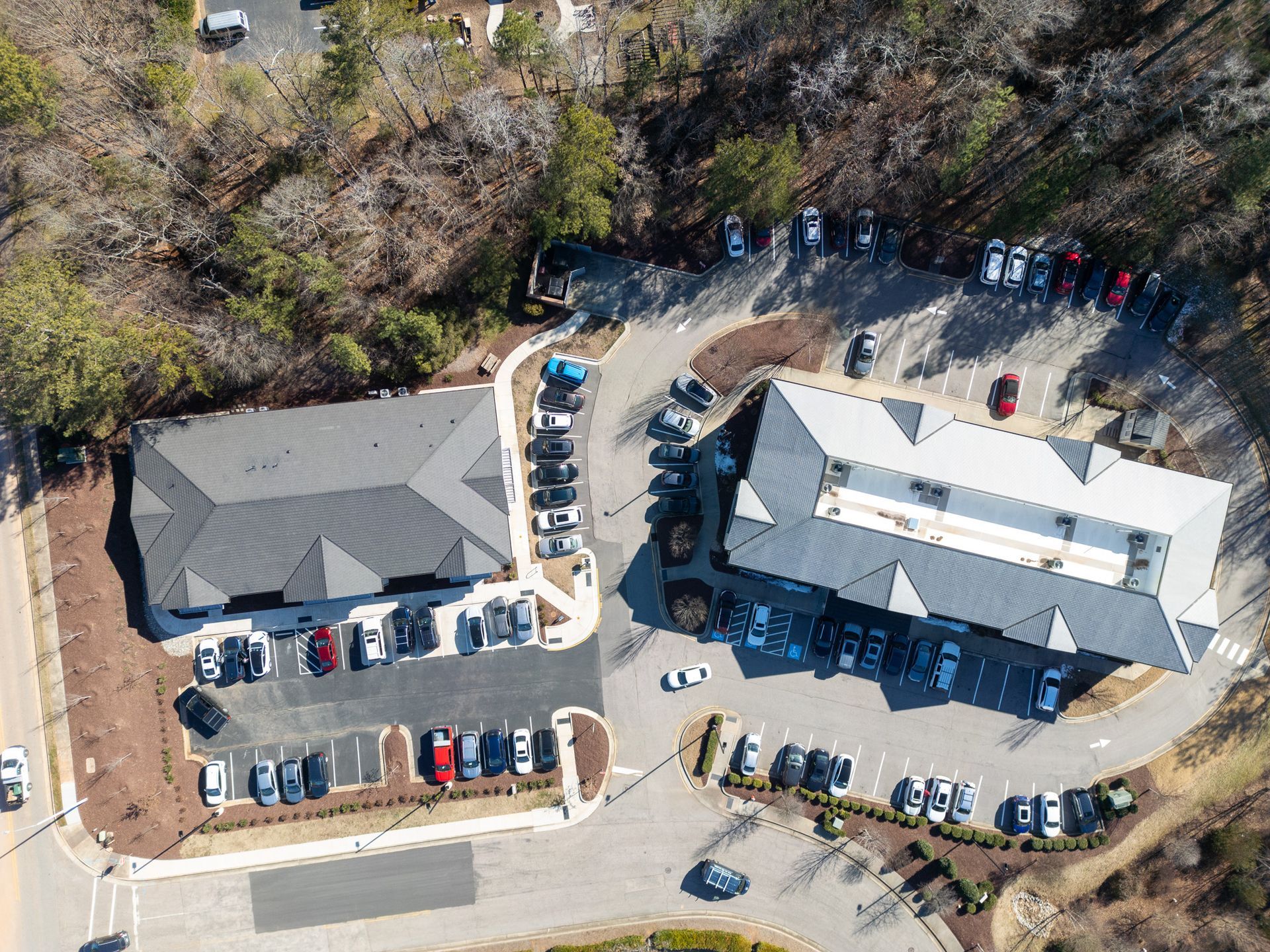 Aerial view of two office buildings with parking lots, surrounded by trees.