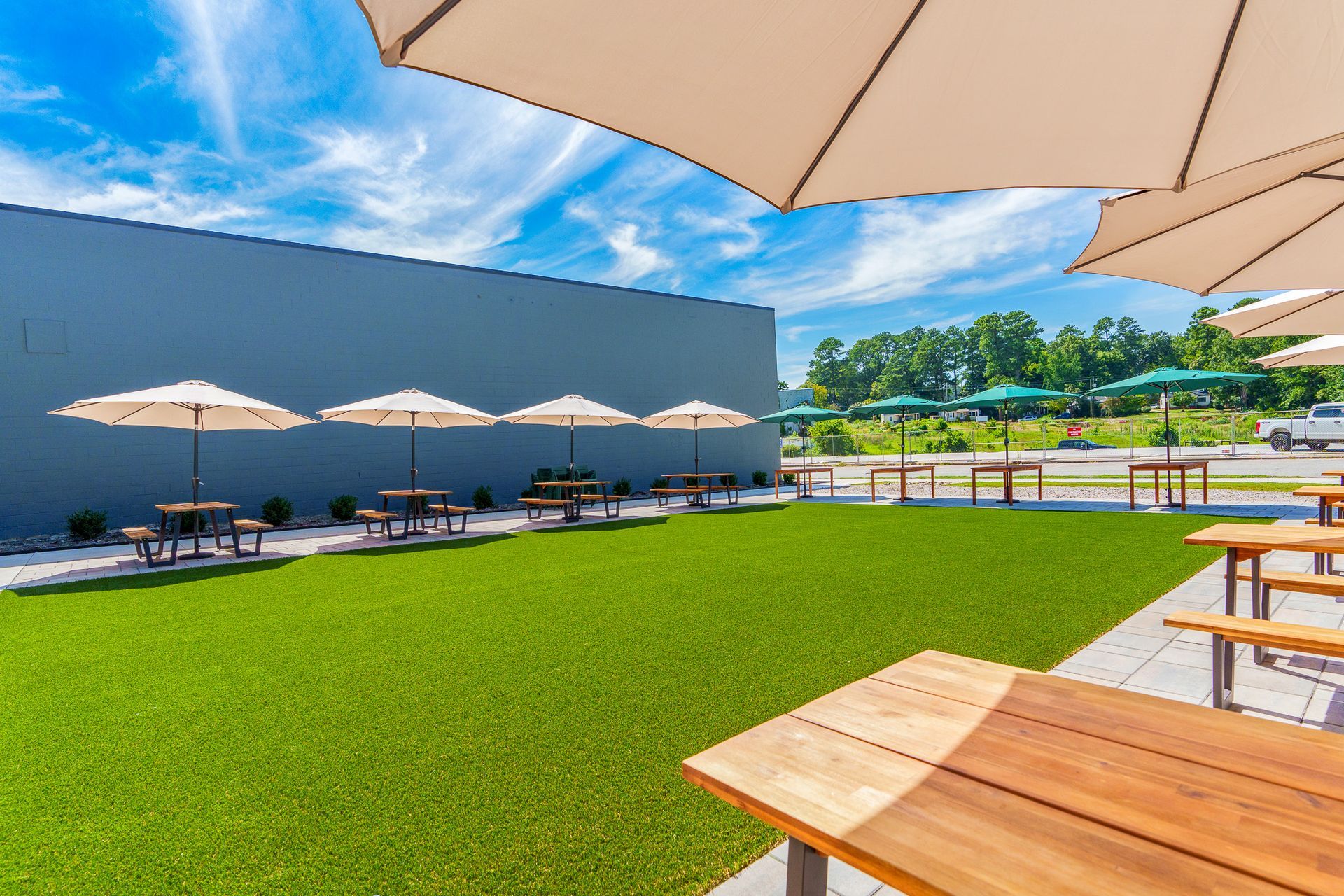 Outdoor dining area with tables, umbrellas, and green turf against a blue sky.