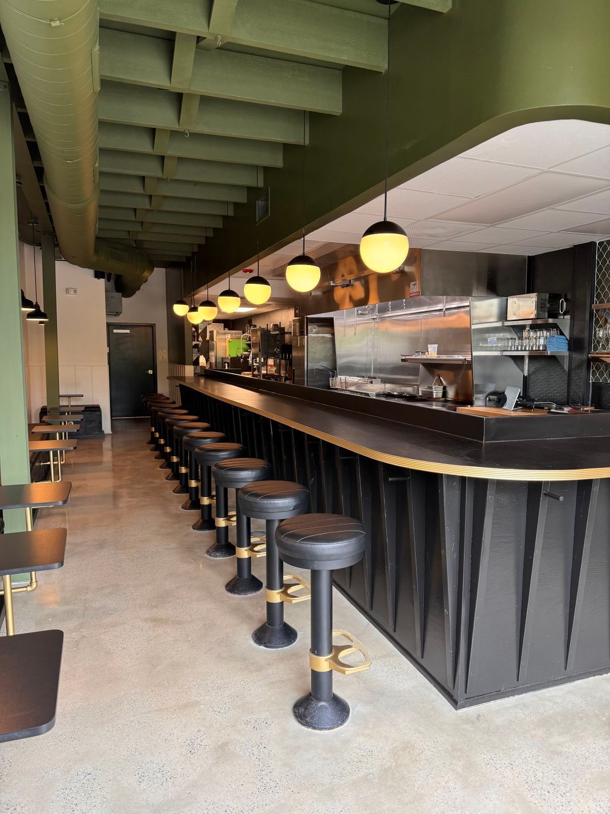 Interior of a restaurant with black bar stools, counter, and olive green accents.