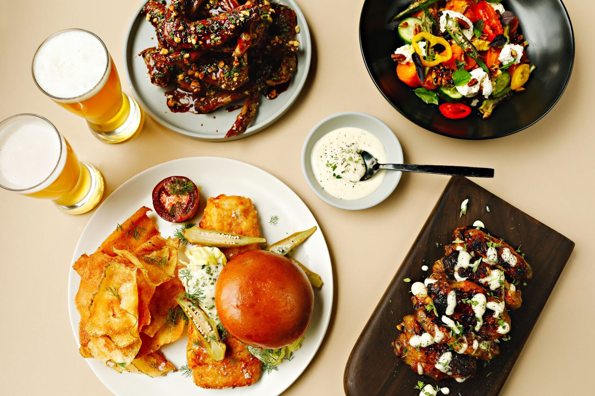 Overhead shot of various dishes: ribs, salad, burger, wings, chips, beer.