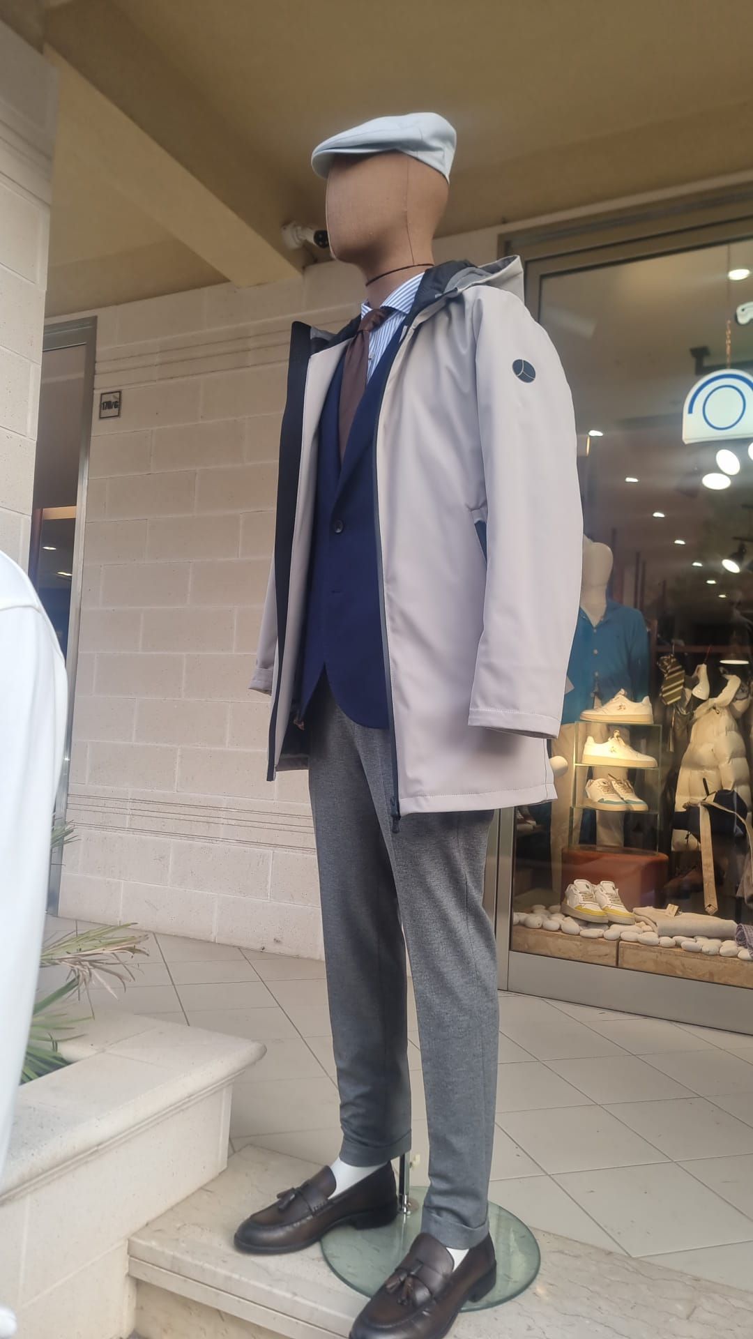 Un manichino che indossa una giacca e un cappello è in piedi davanti a un negozio.