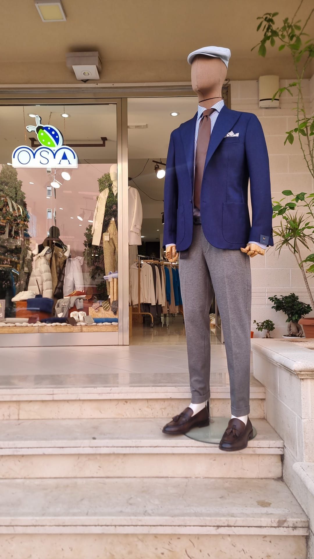 Un manichino che indossa una giacca blu e pantaloni grigi è in piedi davanti a un negozio.