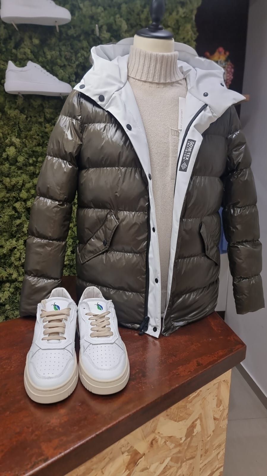 Una giacca e delle scarpe da ginnastica sono appoggiate su un tavolo di legno accanto a un manichino.