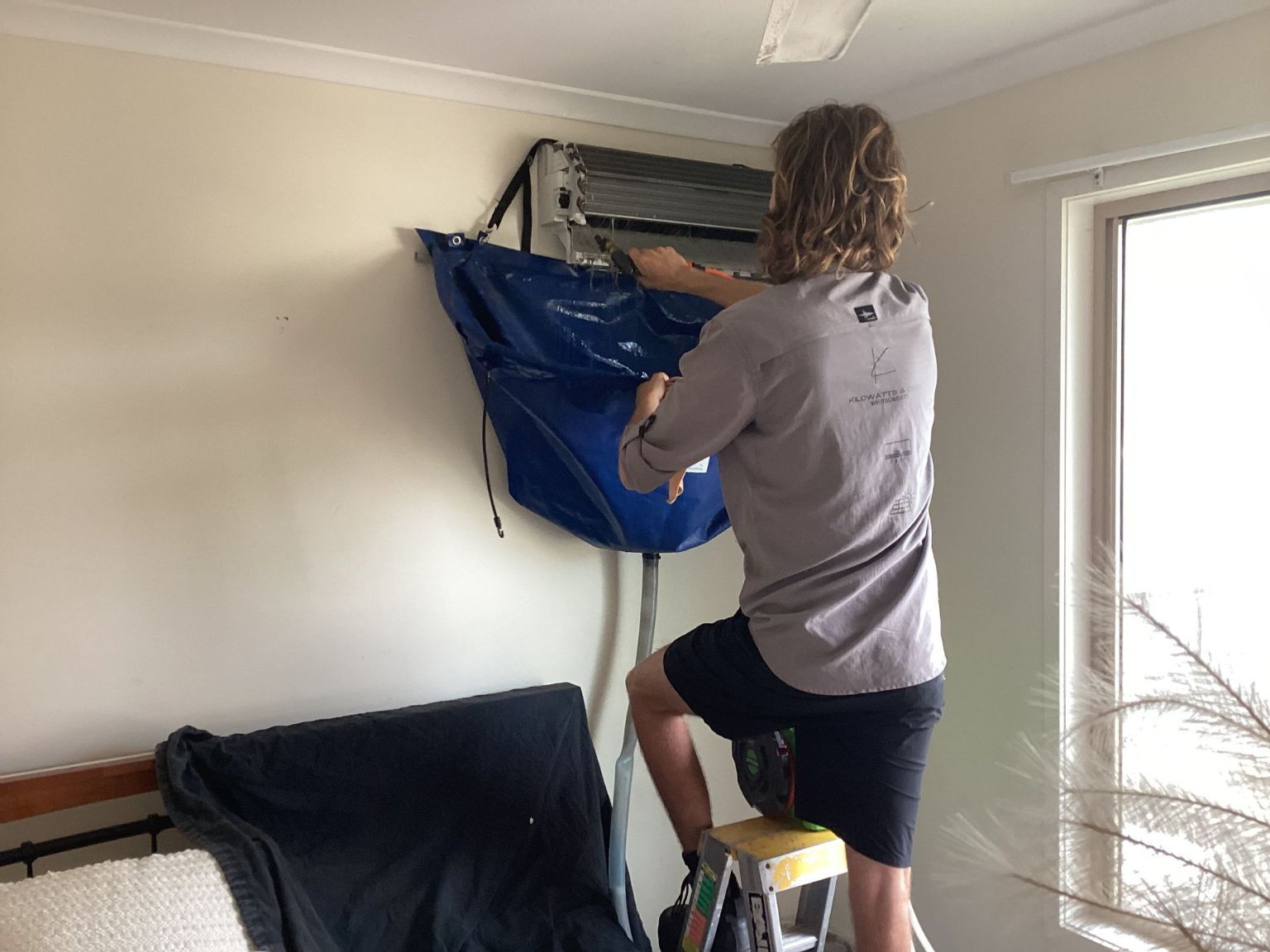 A Man is Cleaning an Air Conditioner in a Living Room — Kilowatts & Cool Whitsundays In Strathdickie, QLD
