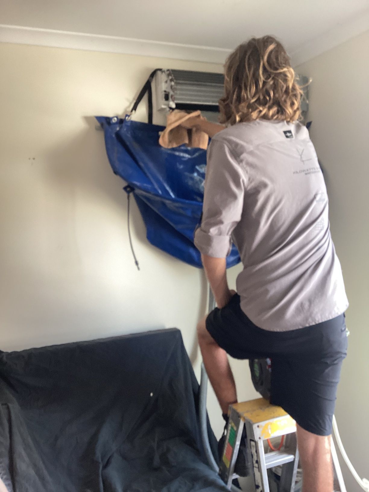 A Man Cleaning an Air Conditioner With a Blue Tarp — Kilowatts & Cool Whitsundays In Airlie Beach, QLD
