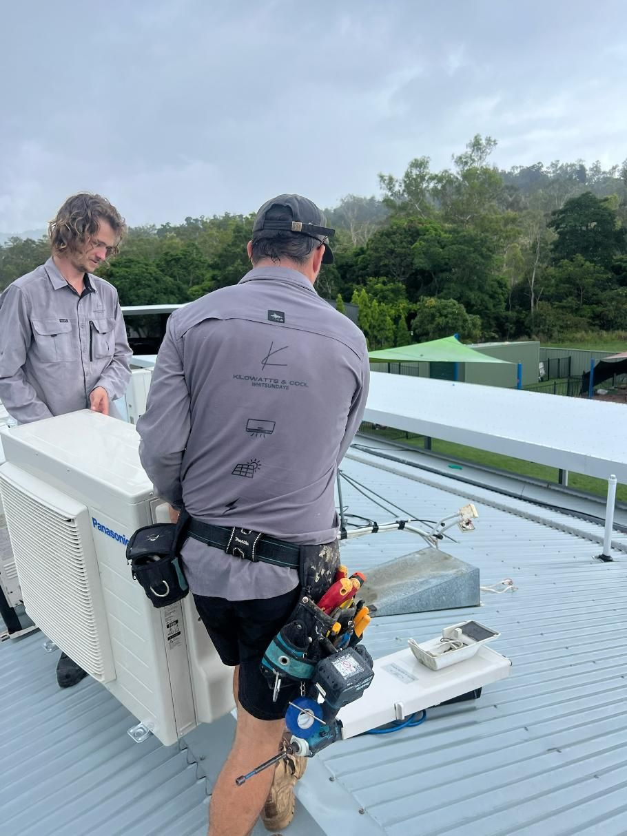 Two Men Are Standing on Top of A Roof Carrying a Large Aircon — Kilowatts & Cool Whitsundays In Airlie Beach, QLD